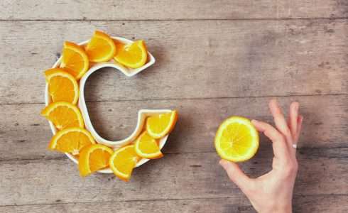 A hand is about to pick up a slice from a ceramic plate shaped like a C, which is artistically arranged with orange slices on a wooden surface in Idaho.