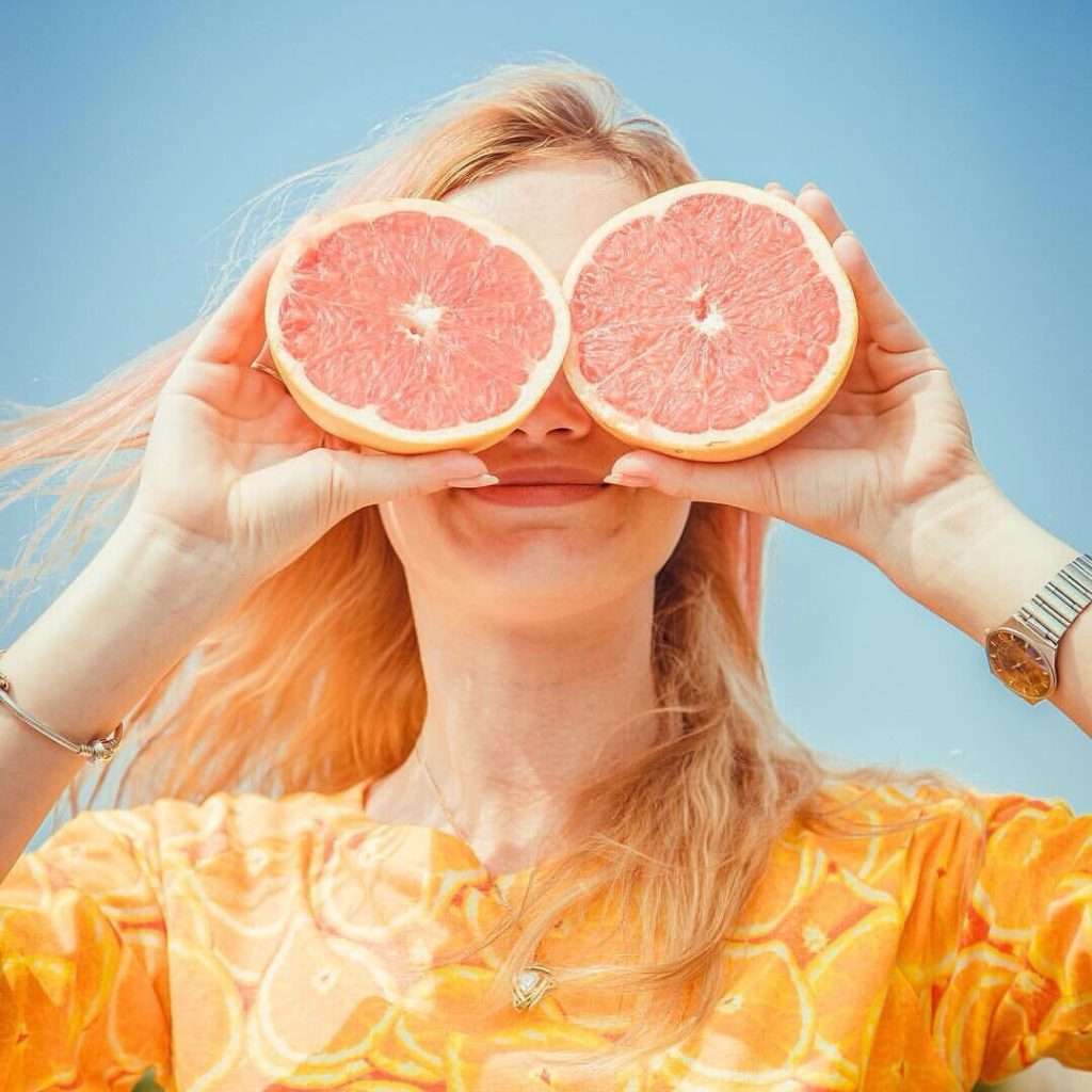 Woman holding grapefruit halves in front of her eyes against a blue sky background, symbolizing the importance of functional medicine in maintaining health.
