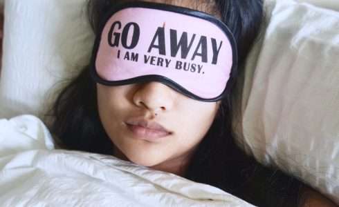 A person resting in bed in Meridian, Idaho, with a sleep mask that reads "go away I am very busy.