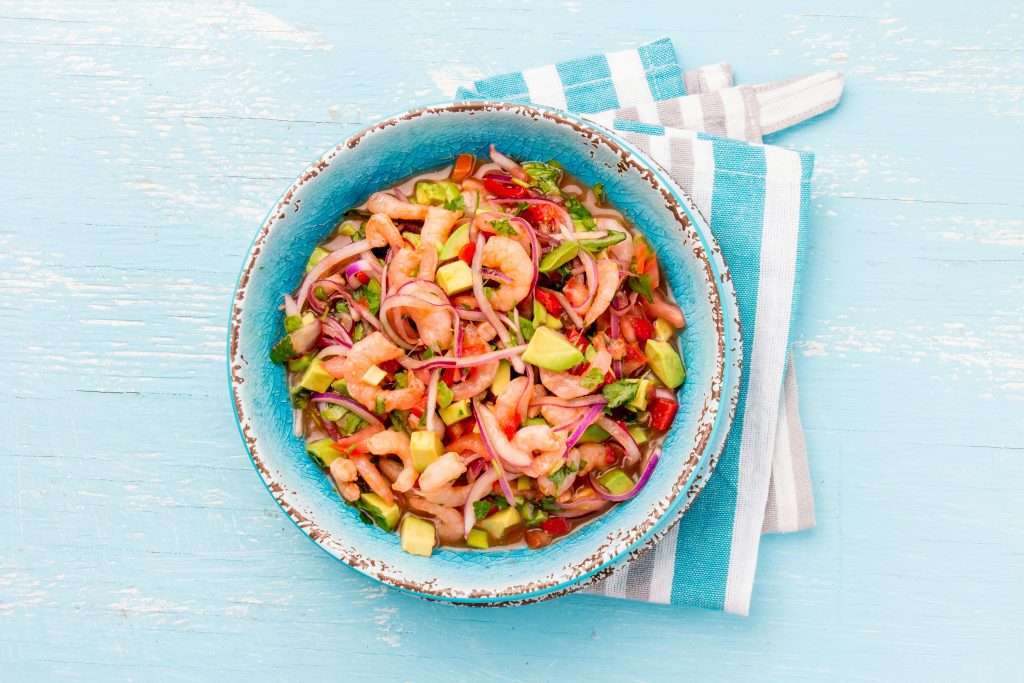 A colorful shrimp avocado salad served in a blue bowl on a wooden surface with a striped napkin, inspired by Boise's naturopathic medicine principles.