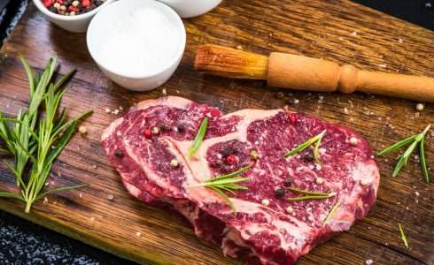 Raw steak in the shape of a heart seasoned with peppercorns and herbs on a wooden cutting board, celebrated by functional medicine enthusiasts in Boise.