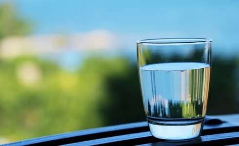 A clear glass of water on a railing with a blurred naturopathic medicine background.