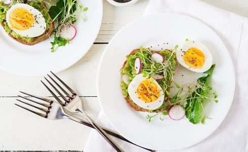 Open-faced sandwiches topped with avocado, radishes, greens, and a boiled egg on white plates, inspired by naturopathic medicine principles.