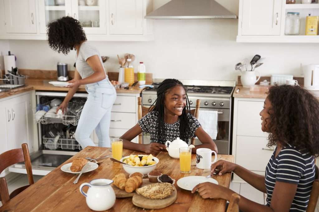 A family enjoying breakfast together in a bright kitchen, with one person washing dishes and two others sitting at the table discussing the benefits of IV therapy.