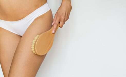 Woman using massage brush for skin health.