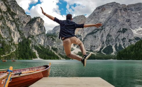 Rear view of man jumping on wooden deck by lake. Happy person in idyllic place in nature.