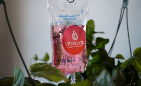 A pink liquid-filled Virasoap pouch hangs among green leaves, showcasing its bold branding on the front. Discover the dynamic benefits of NAC infused within, promising a rejuvenating experience with every use.