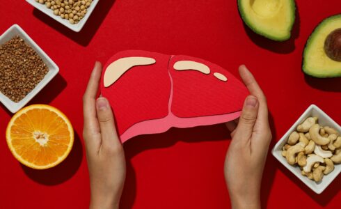 Paper mockup of liver in female hands and food on red background, top view